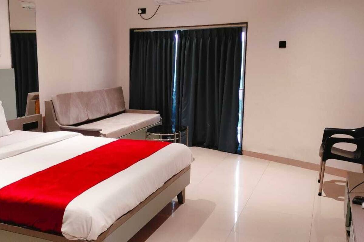 Ein Hotelzimmer mit Bett, Schreibtisch, Stuhl, Fernseher und einem Fenster mit Vorhängen.