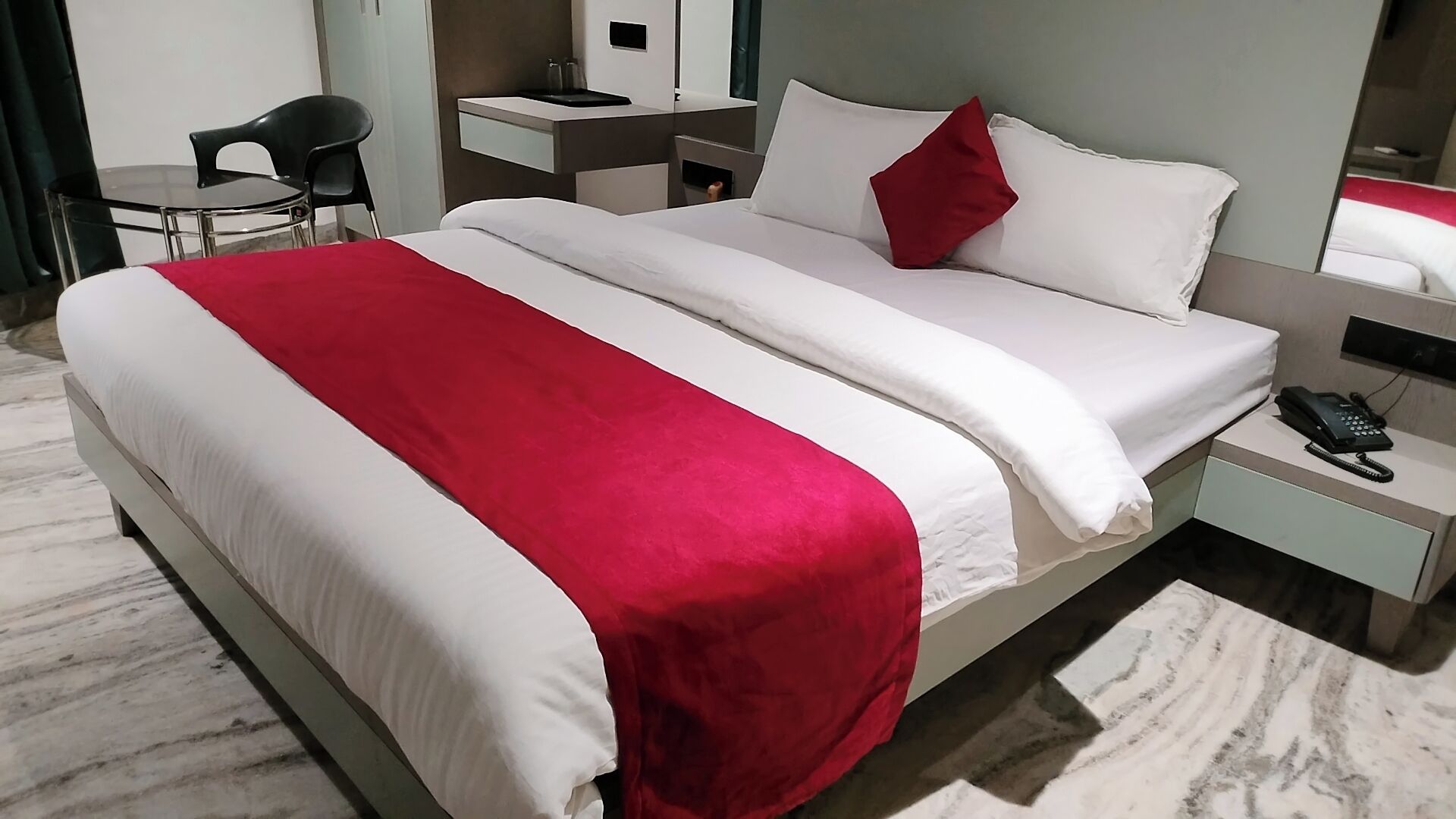 A hotel room with a bed, a desk, a chair, a nightstand, and a telephone.