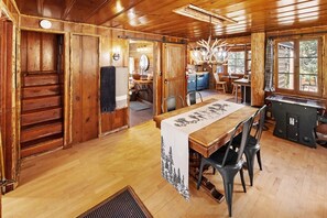 A wooden interior with a dining table, chairs, a kitchen area, and a large window.