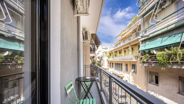 A balcony with a table and chairs, a window, and a view of adjacent buildings. - 2BRCozy Urban Retreat Exarchia (Athens)