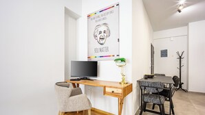 A modern living room with a wooden desk, a television, a green desk lamp, and a dining area with patterned chairs. - 2BRCozy Urban Retreat Exarchia (Athens)