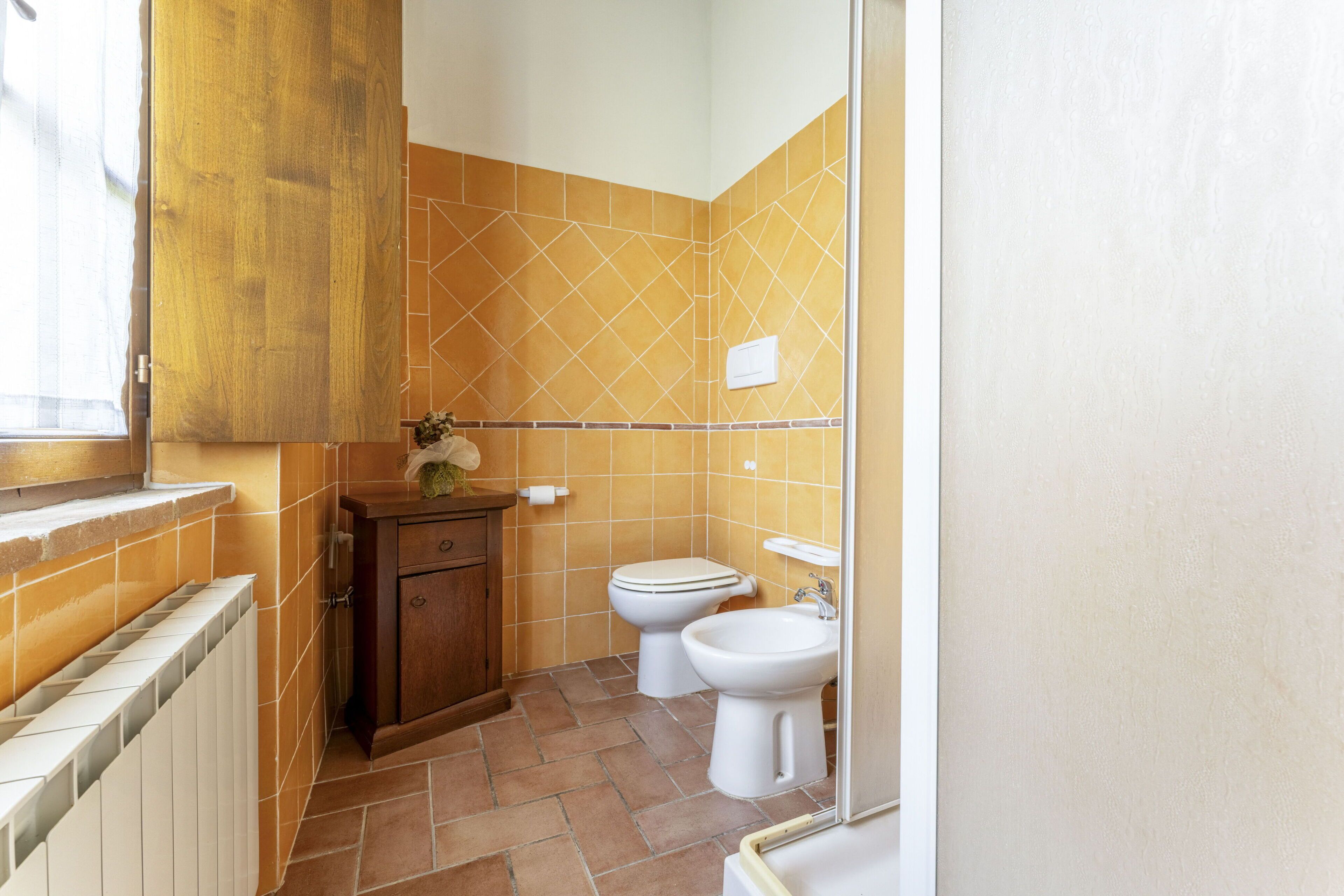 Un baño con un mueble de madera, un inodoro, un bidé y un radiador.