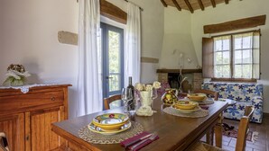 A dining area with a wooden table set for a meal, a sofa with a floral pattern, and a fireplace. - Marcigliana Cottage, Pool, Radicondoli (Radicondoli)
