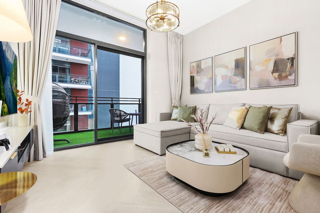 A modern living room with a sofa, coffee table, and artwork. A balcony with a view of a building is visible.
