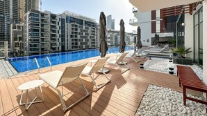 A rooftop pool area with lounge chairs and umbrellas, surrounded by modern buildings and a clear sky. - FIRST CLASS | 2BR | Serene Retreat in Wilton (Dubai)