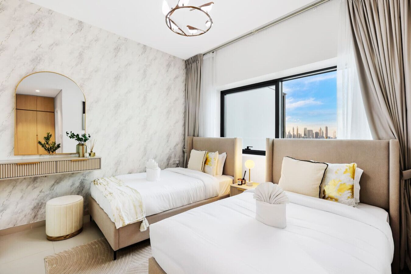 Une chambre d’hôtel moderne avec deux lits, une grande fenêtre donnant sur la ville, un mur en marbre et un miroir avec un cadre doré.