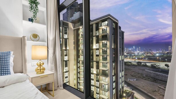 A modern hotel room with a large window overlooking a cityscape at dusk. - FIRST CLASS | 2BR | Serene Retreat in Wilton (Dubai)