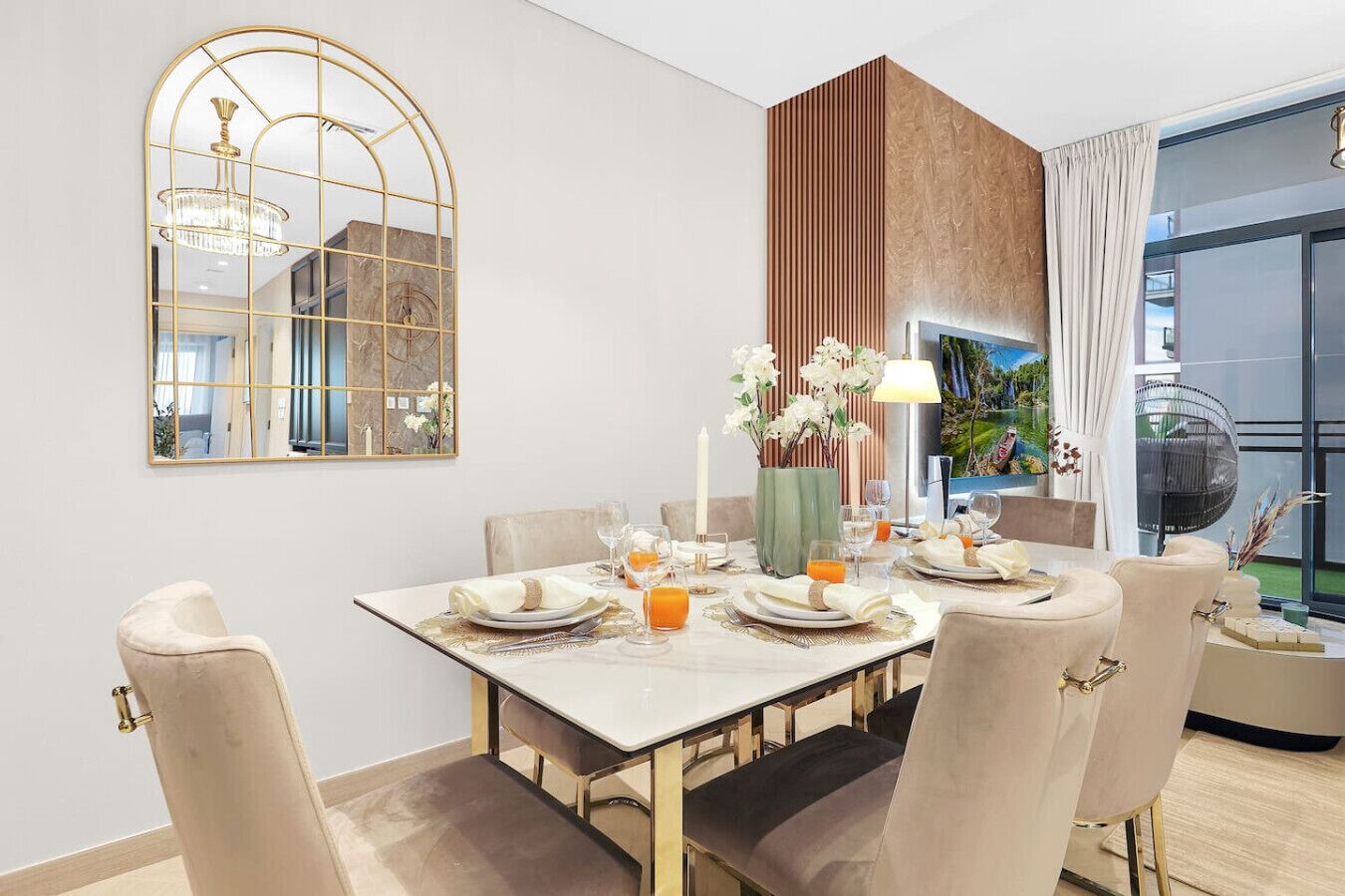 Un coin repas avec une table dressée pour quatre personnes, un lustre, un miroir et une vue sur l’extérieur.
