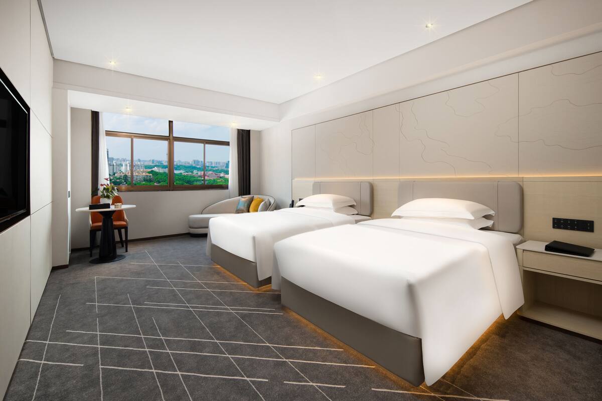 Habitación de hotel moderna con dos camas, un escritorio y vistas a la ciudad.