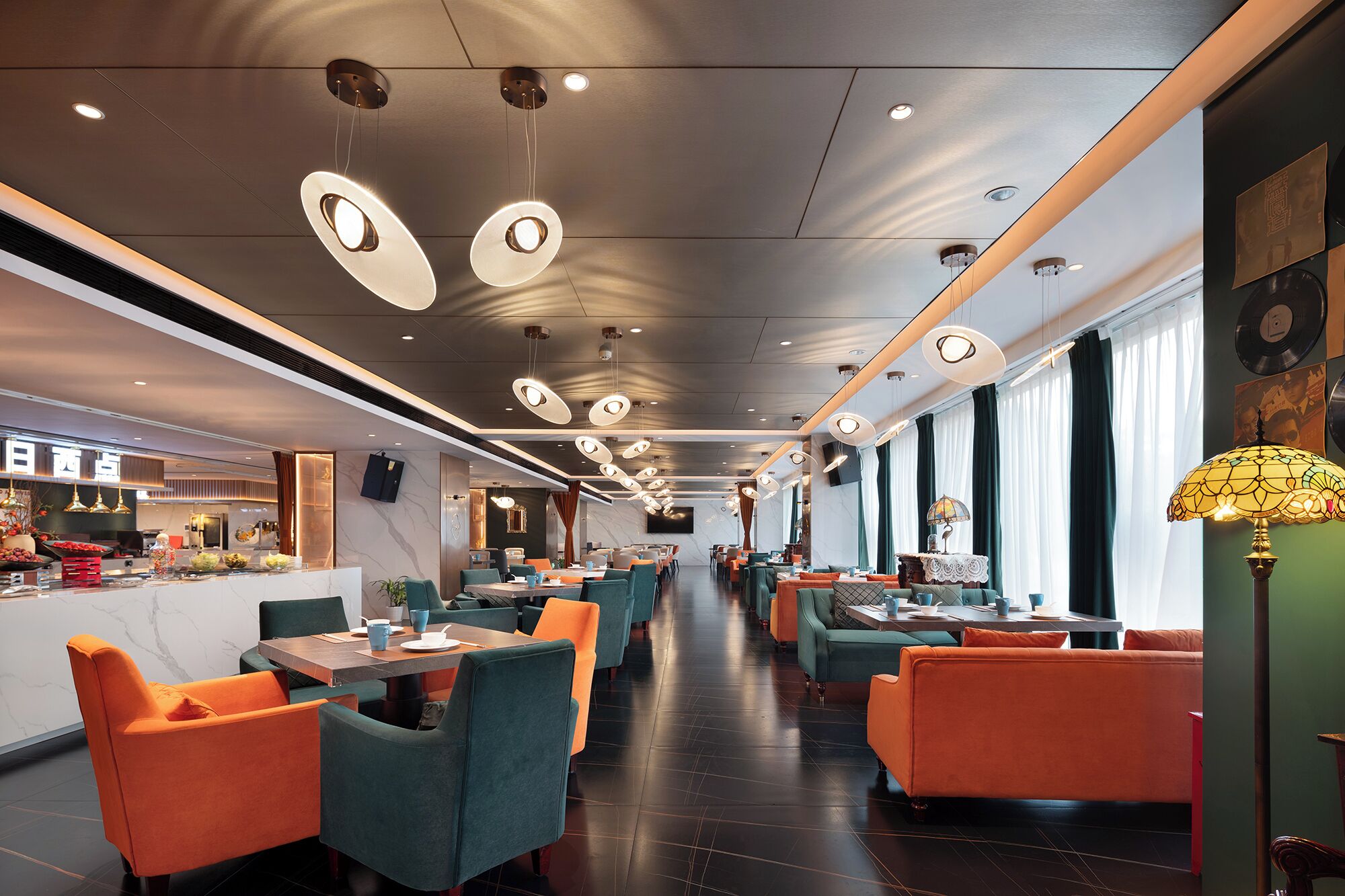 Ein modernes Restaurantambiente mit hohen Decken, Pendelleuchten und verschiedenen Sitzmöglichkeiten.