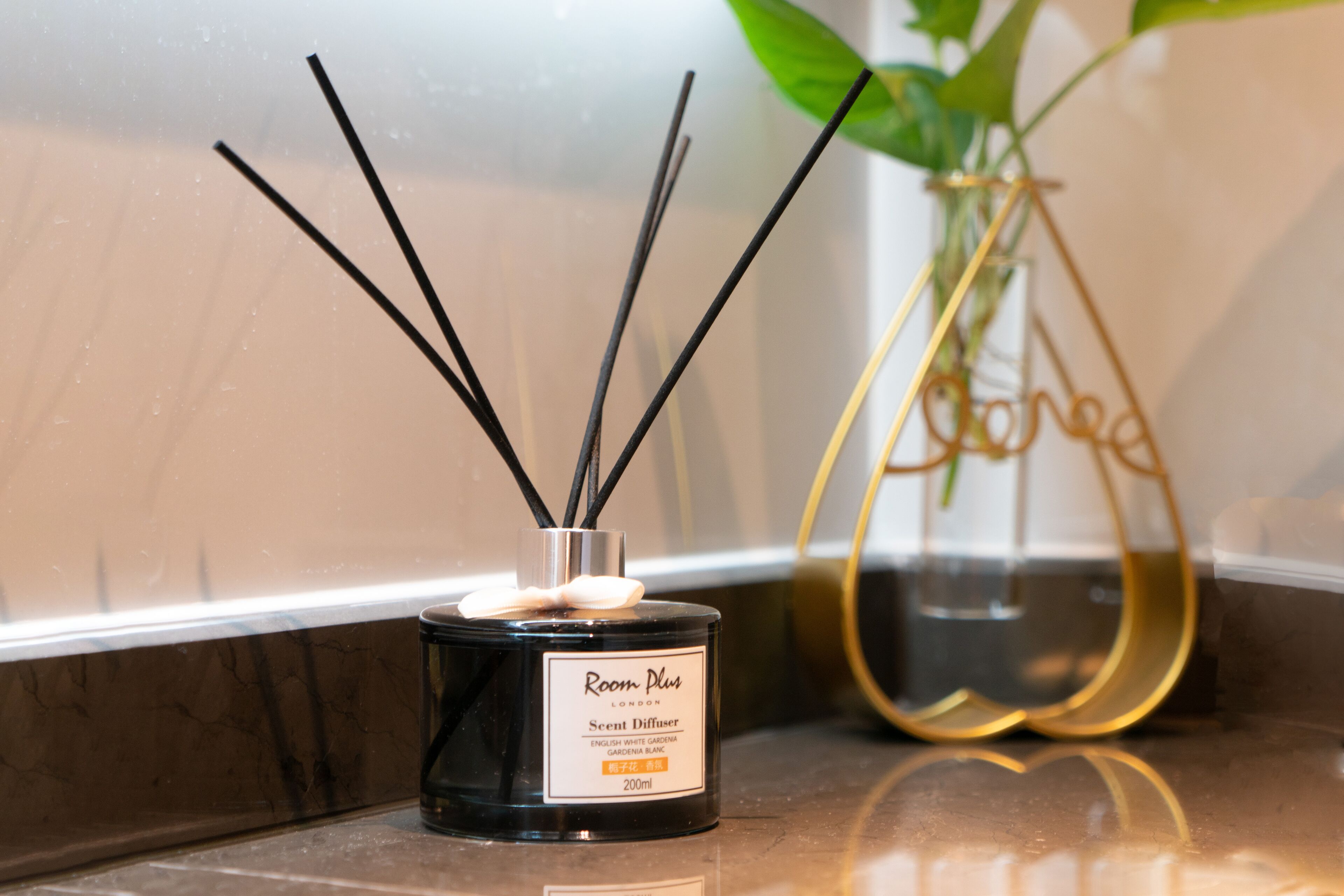 A black diffuser with reed sticks and a label, placed on a reflective surface.