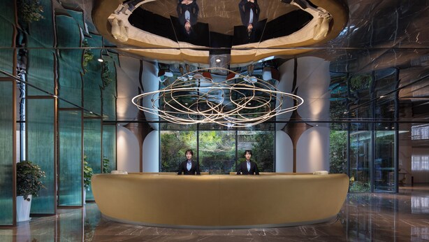 A reception area with a modern design, featuring a central desk, two receptionists, and a unique ceiling structure. - Li Gao Exclusive Hotel (Changsha)