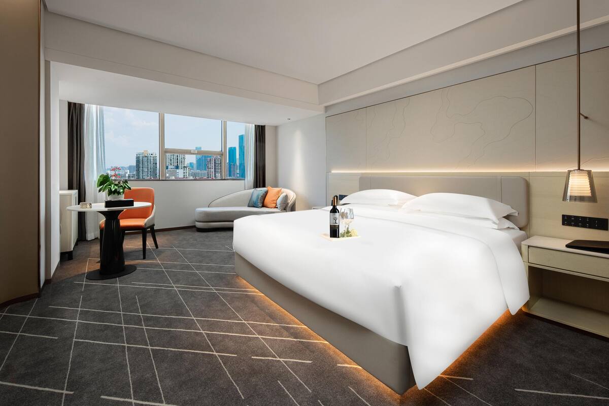 Una habitación de hotel moderna con una cama grande, un escritorio, una silla y vistas del horizonte de la ciudad.