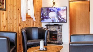 A cozy living room with a stone fireplace, leather armchairs, a wooden coffee table, and a flat-screen TV mounted on the wall. - Dominic by Interhome (Nendaz)