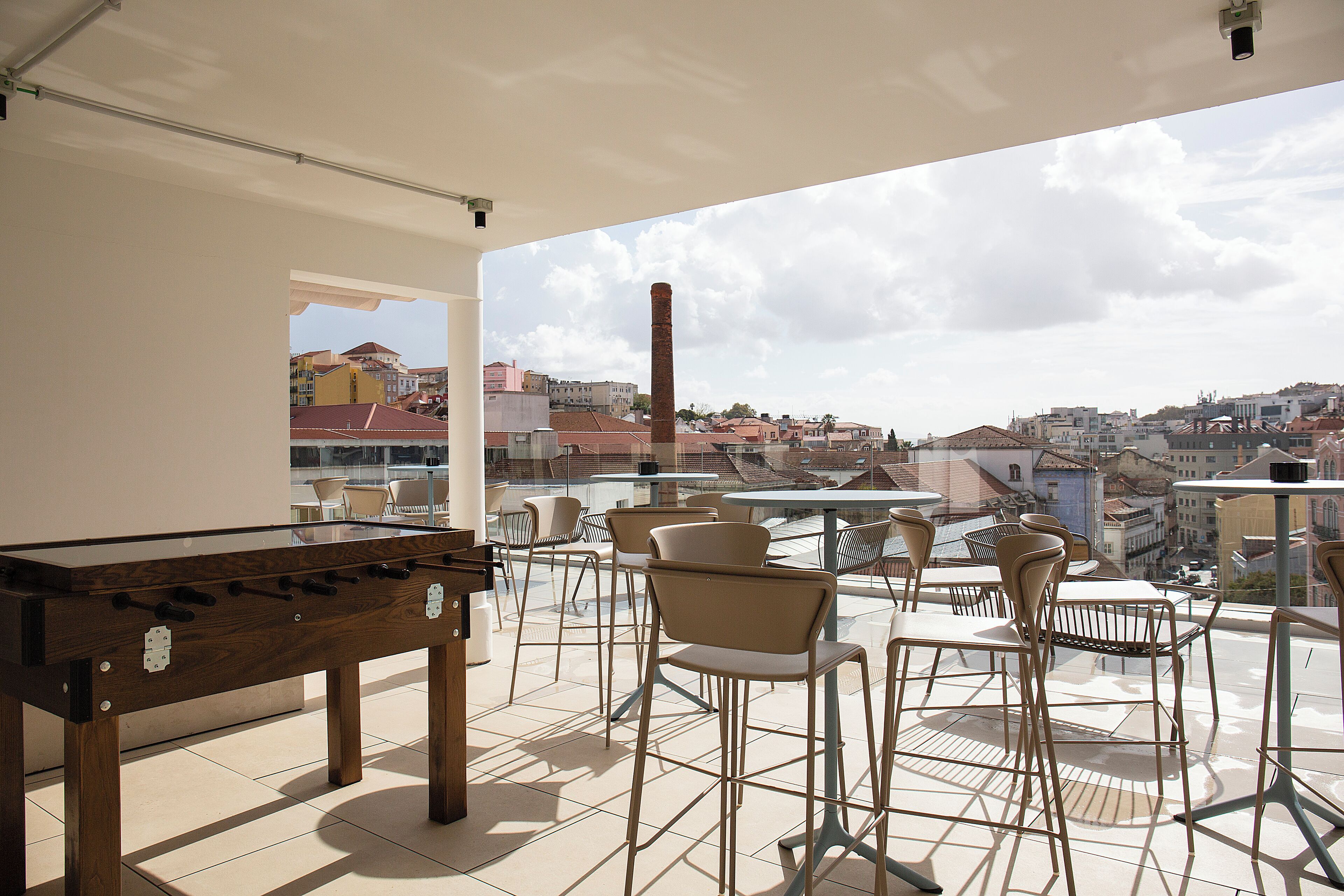 A rooftop terrace with a foosball table, chairs, and a view of a cityscape.