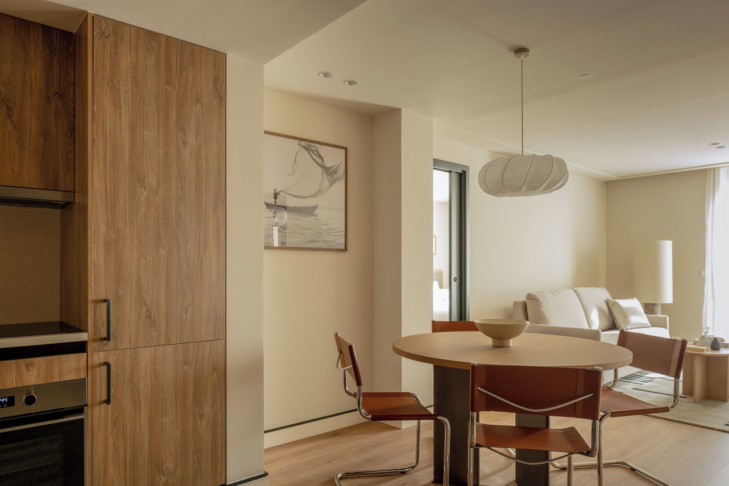 A modern kitchen with wooden cabinets, a dining area with a round table and chairs, and a large window providing natural light.