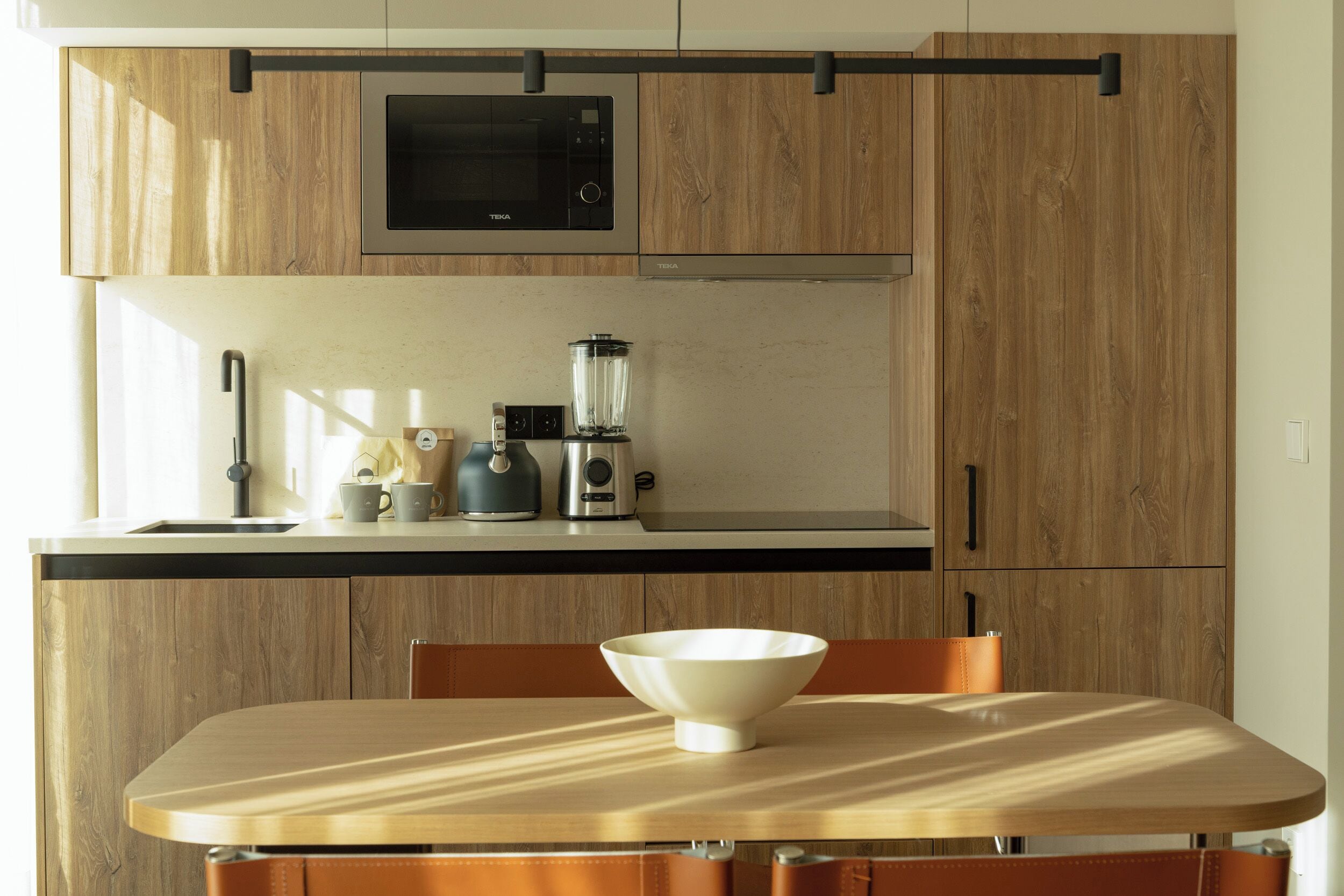 A kitchen with wooden cabinets, a black microwave, a blender, and a white bowl on the counter.
