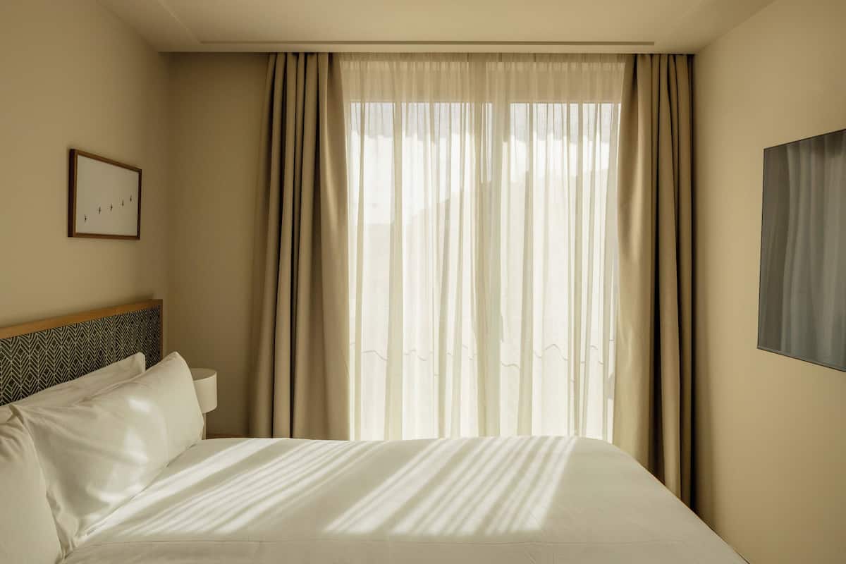 A hotel room with a bed, curtains, a headboard, a wall-mounted picture, and a painting.