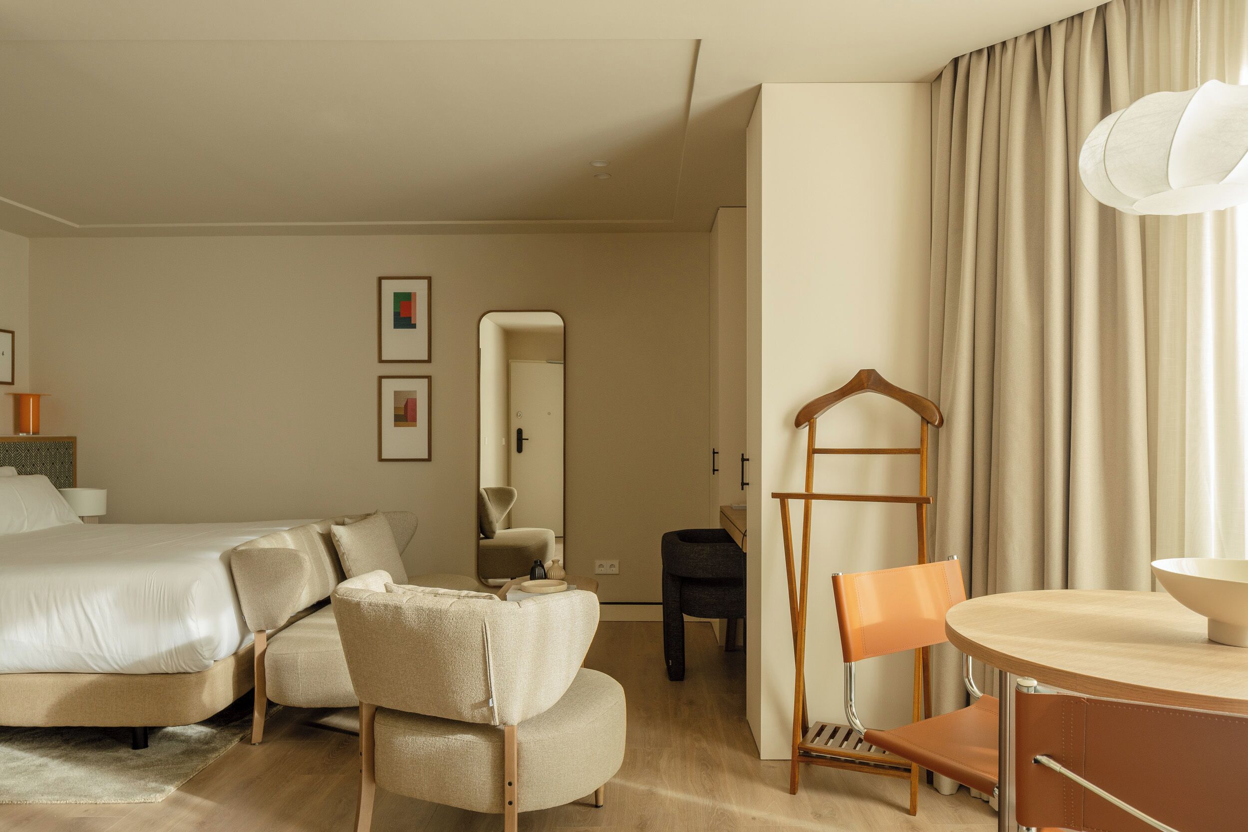 A hotel room with a bed, a chair, a table, a mirror, and a hanging light fixture.