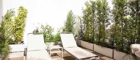 A patio area with three sun loungers, a small table, and potted plants.