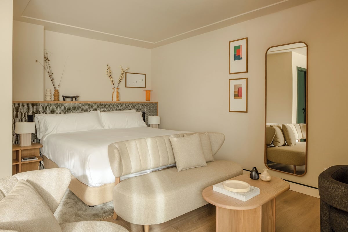 A modern hotel room with a large bed, a sofa, a small table, and a mirror.