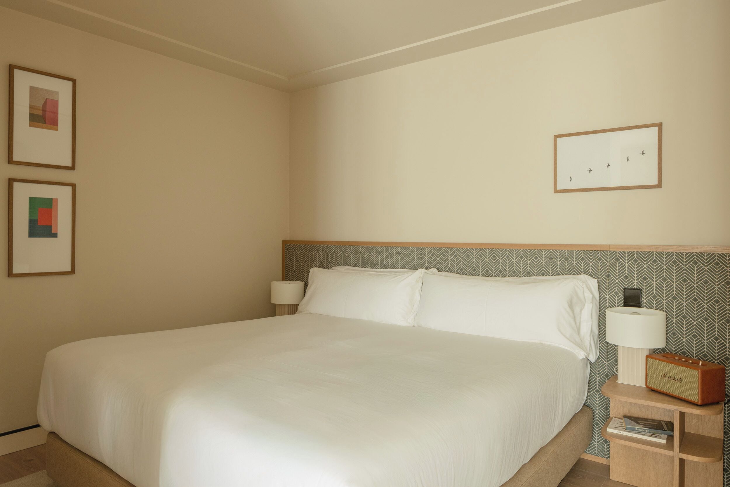 Un lit bien fait dans une chambre d’hôtel, avec une tête de lit, deux lampes de chevet et une table de chevet sur laquelle se trouve une radio.