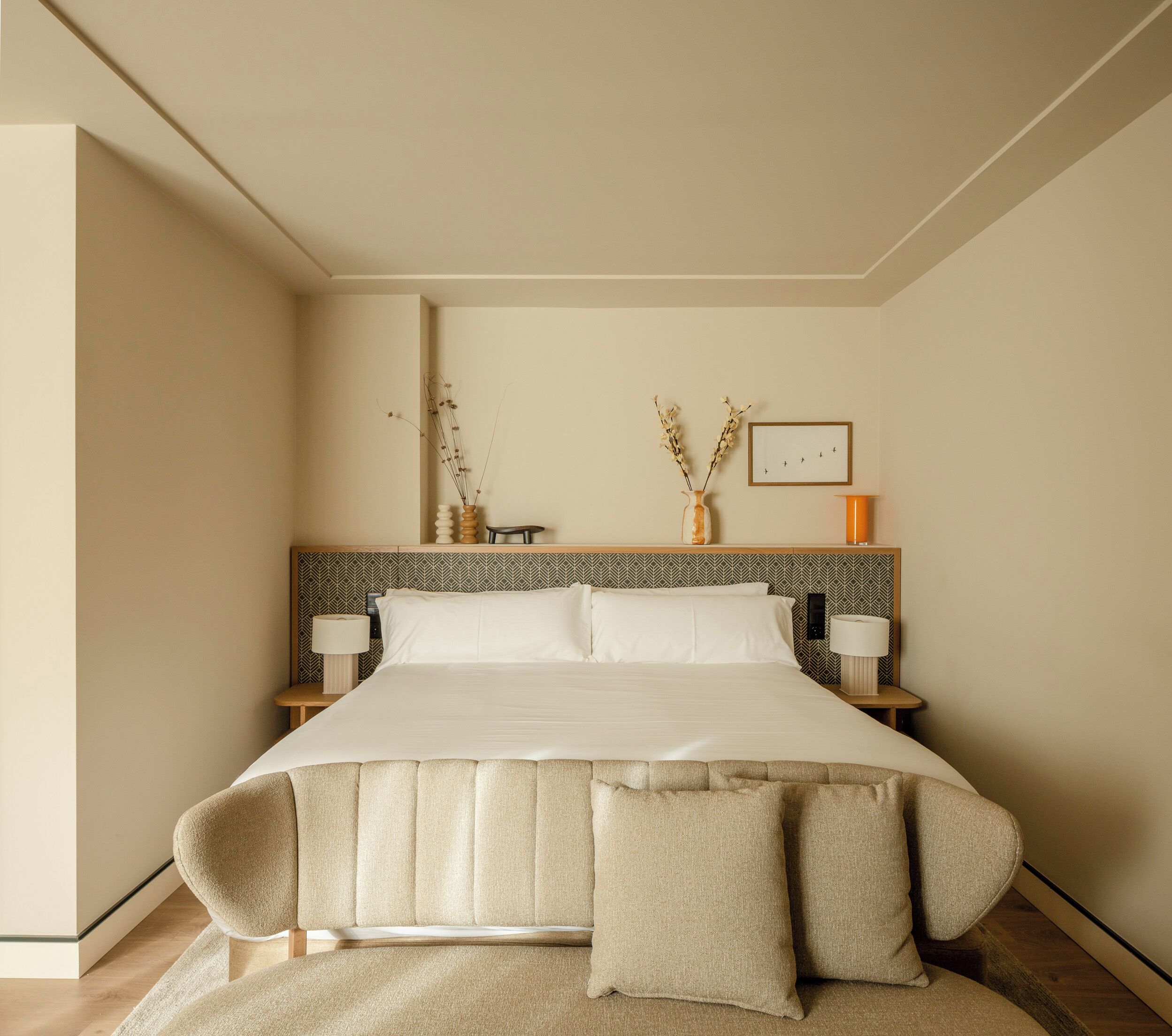 Cama bem arrumada com cabeceira, duas mesas de cabeceira com luminárias e um quadro na parede.