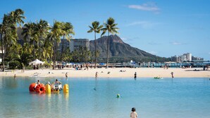 Ein Strand mit Palmen, ein Berg im Hintergrund und ein klarer Himmel.