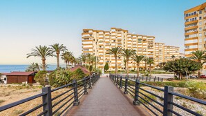 A pathway leading to a beachfront hotel with multiple floors, palm trees, and a clear view of the sea. - A&N Algarrobo Beach Tower (Algarrobo Costa)