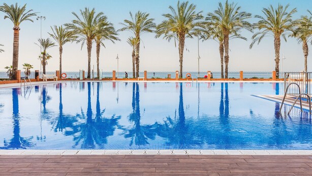 A swimming pool with palm trees and a fence. - A&N Algarrobo Beach Tower (Algarrobo Costa)
