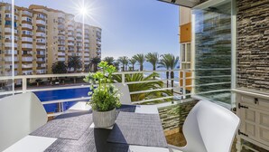 A balcony with a view of a swimming pool, palm trees, and a building in the background. - A&N Algarrobo Beach Tower (Algarrobo Costa)