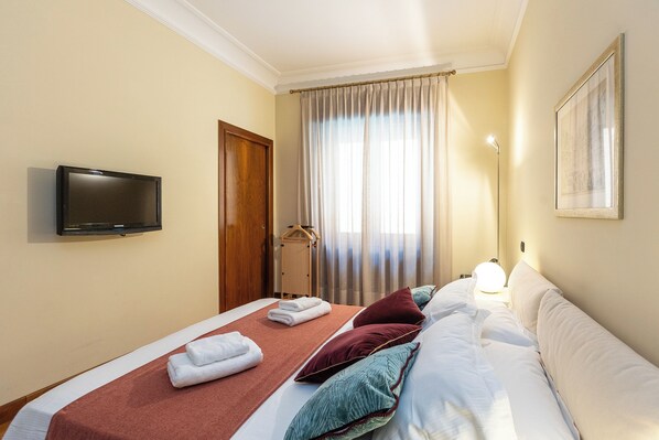 A hotel room with a bed, a television, a door, and a window with curtains.