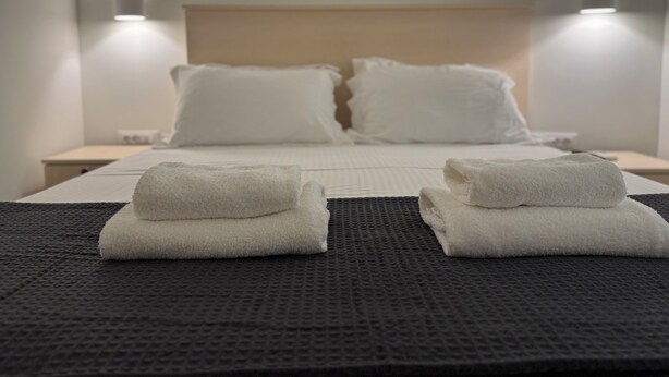A hotel room with a bed, two bedside lamps, and two folded towels on the bed. - Cozy appartment at the heart of the Historic center - Hermes Central Suite (Αθήνα)