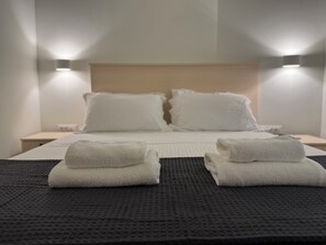 A hotel room with a bed, two bedside lamps, and two folded towels on the bed.