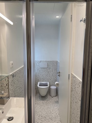 Een badkamer met toilet, bidet en een douchecabine met glazen wanden.