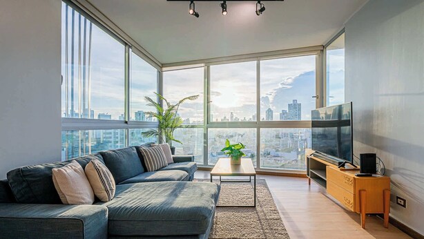A modern living room with a large window, a sofa, a coffee table, a TV, and a plant. - w* | Airy 2BR in San Francisco w/ Pool (Panamá)