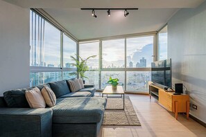 A modern living room with a large window, a sofa, a coffee table, a TV, and a plant.