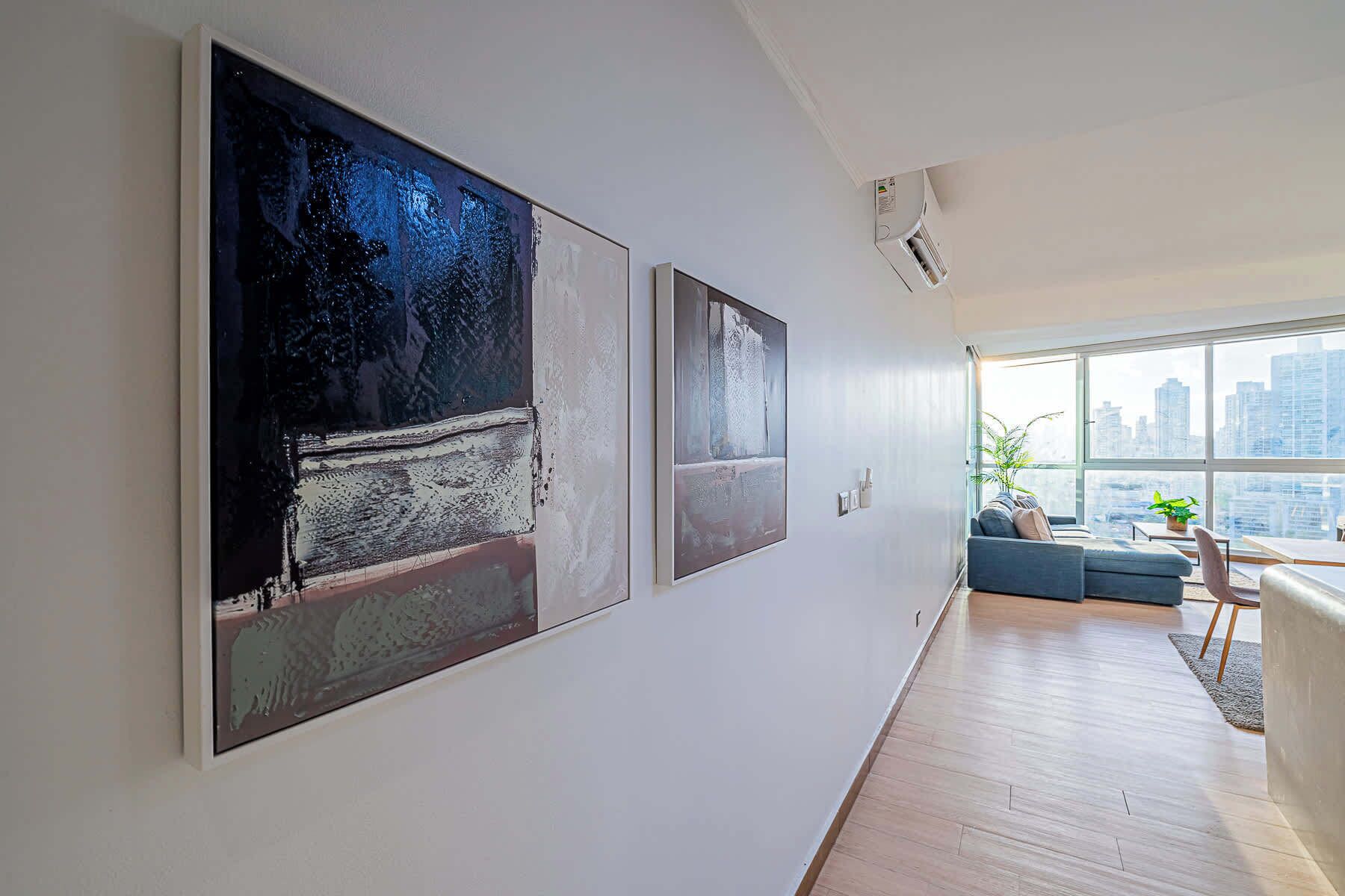 Un salon moderne avec une grande fenêtre, un canapé et des œuvres d’art abstraites accrochées au mur.