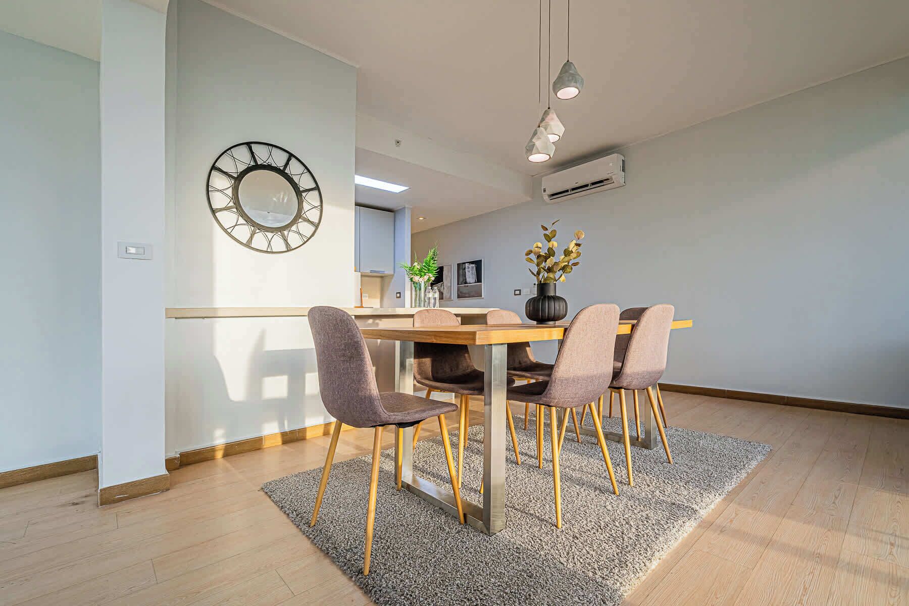 A modern dining area with a wooden table, four chairs, a decorative vase, and a wall-mounted clock.