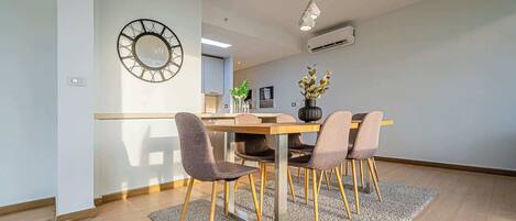 A modern dining area with a wooden table, four chairs, a decorative vase, and a wall-mounted clock.