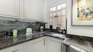 Une cuisine moderne avec des meubles blancs, un plan de travail en marbre et une fenêtre donnant sur un immeuble en briques.