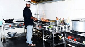 A chef in a professional kitchen with stainless steel appliances, pots, and cooking utensils. - Sai Baba Palace Lodging and Boarding (Bidar)