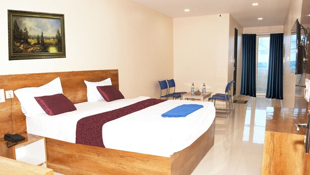 A hotel room with a wooden bed, a desk, chairs, a TV, and a painting on the wall. - Sai Baba Palace Lodging and Boarding (Bidar)