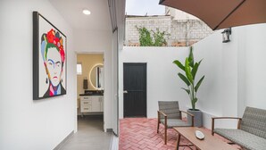 Eine moderne Terrassenanlage mit Ziegelboden, einem Holztisch, zwei Korbstühlen, einem Topfpflanzen und einer schwarzen Tür.
