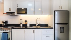 Eine moderne Küche mit weißen Schränken, einem Edelstahl-Kühlschrank, einer Mikrowelle, einem Herd und einem Spülbecken mit Armatur.