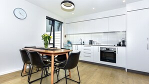 Une cuisine moderne avec des meubles blancs, un four Bosch et un coin repas comprenant une table en bois et des chaises noires.