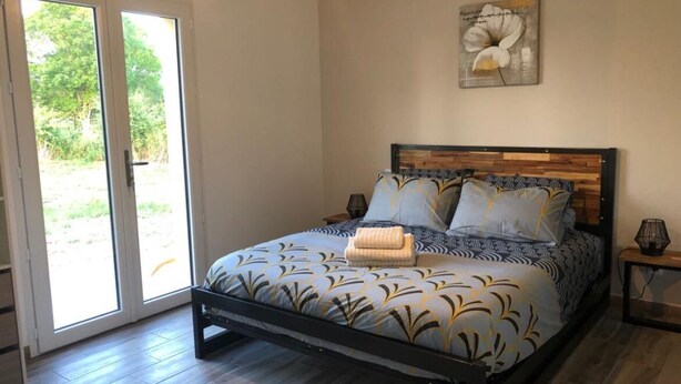 Quarto com cama, cabeceira de madeira, mesa de cabeceira, abajur e um quadro na parede.