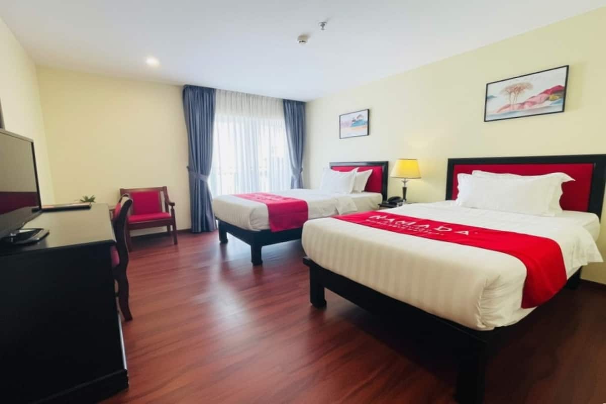 Une chambre d’hôtel avec deux lits, un bureau, une chaise et un téléviseur.