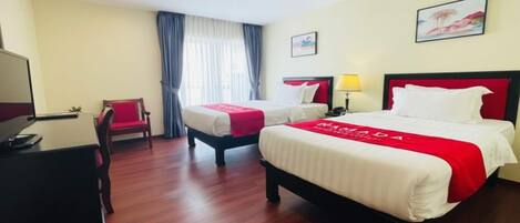 A hotel room with two beds, a desk, a chair, and a television.