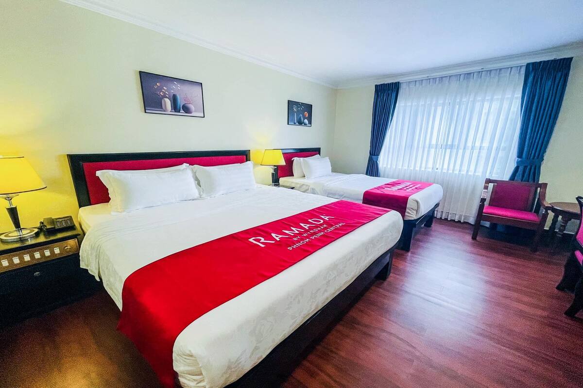 Une chambre d’hôtel avec deux lits, une couvre-lit rouge, une table de chevet avec une lampe et une chaise.
